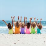 A joyful group of women with hands raised enjoying a sunny day at Santa Monica Beach.
